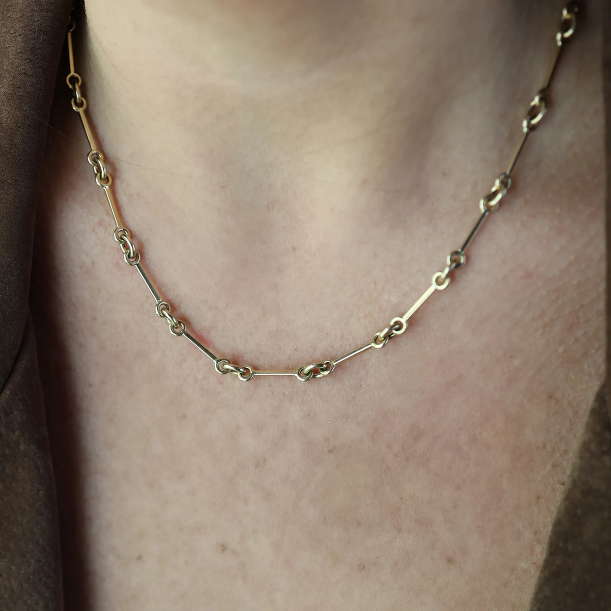 Close-up of the 14k yellow gold horsebit chain necklace at the collarbone, slim gold bars joined by linked rings