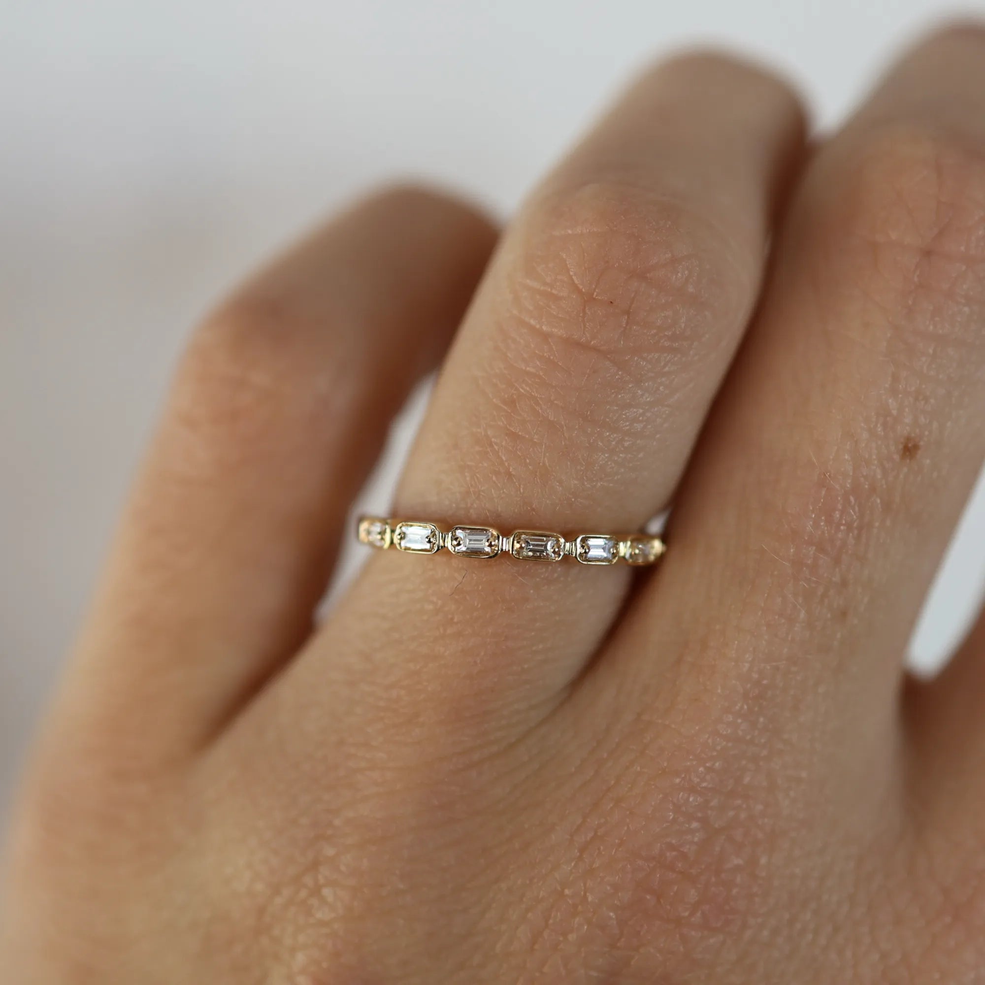 Gold ring with small diamonds on a person's finger against a neutral background