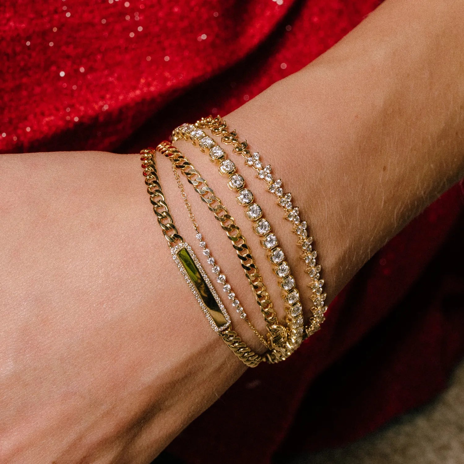 Close-up of a wrist wearing multiple gold bracelets with a red fabric background