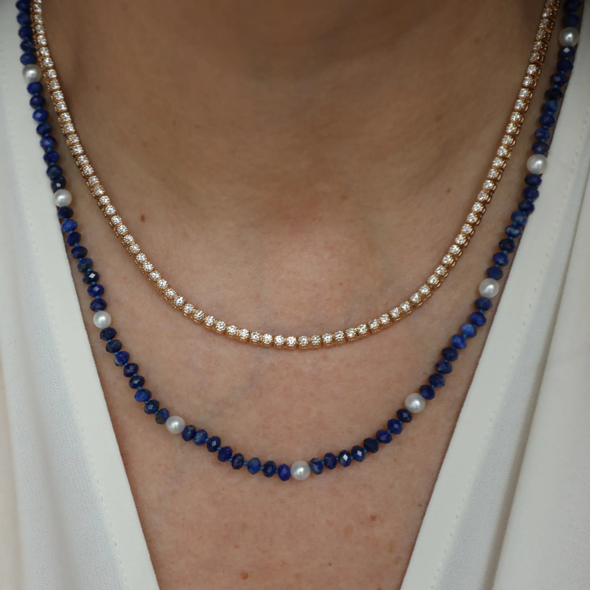 Two necklaces with blue and white beads on a person wearing a white top.