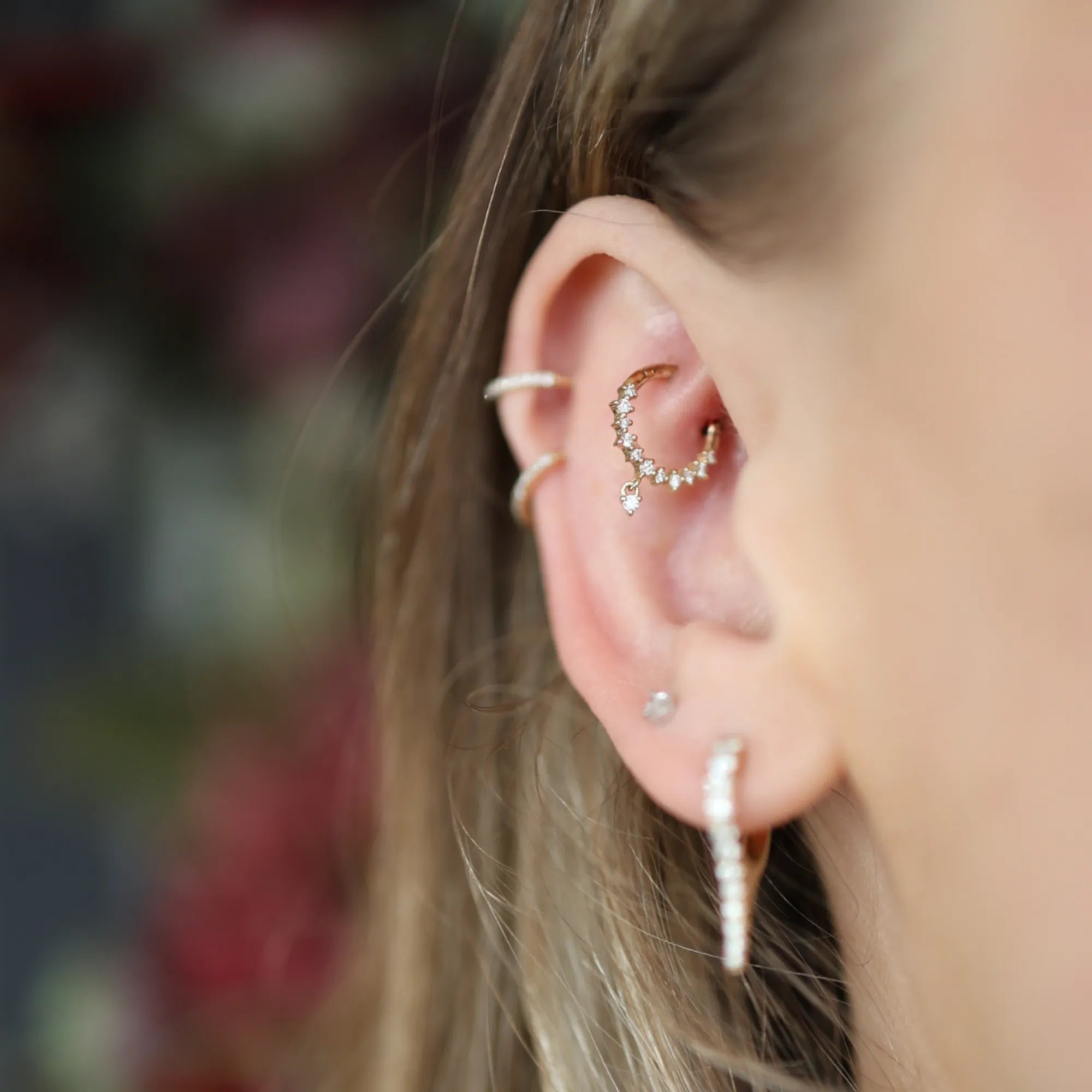 Close-up of an ear with multiple gold earrings against a blurred background