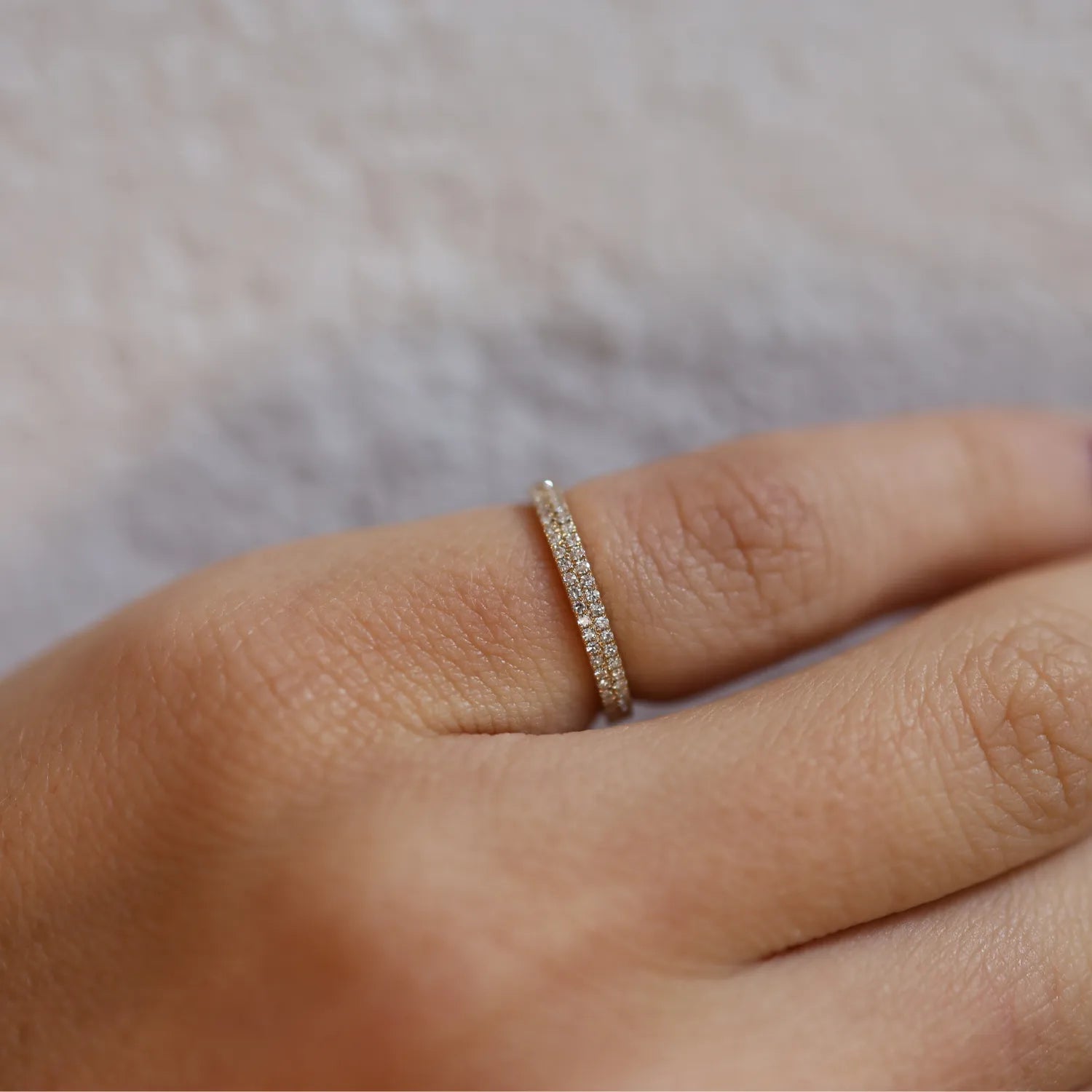 Gold ring with small diamonds on a finger against a neutral background