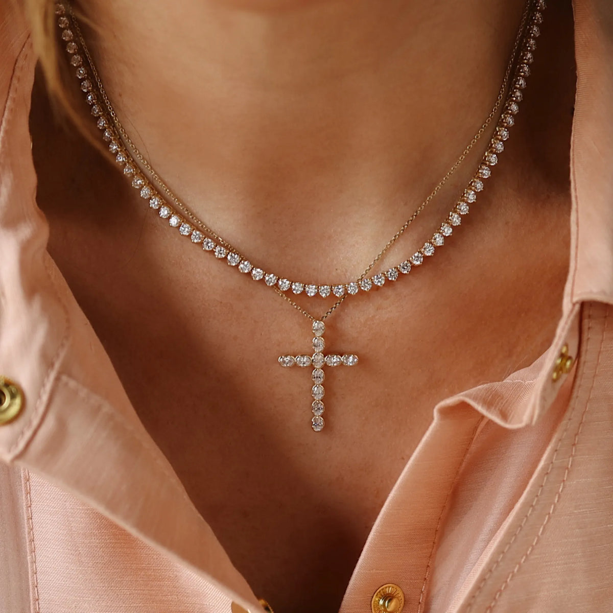 Necklace with a cross pendant worn by a person in a pink shirt.