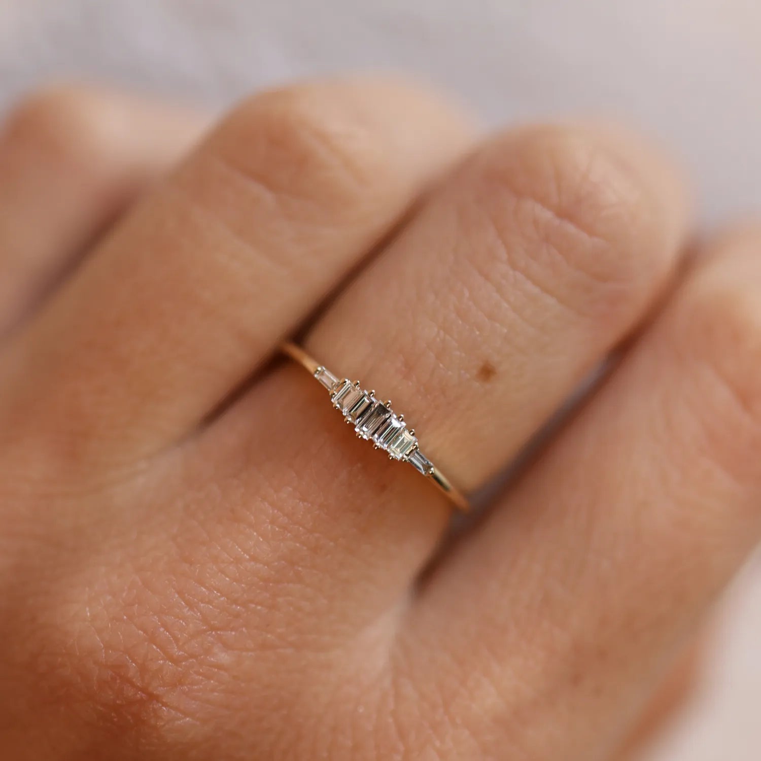 Silver ring with small diamonds on a person's finger against a neutral background