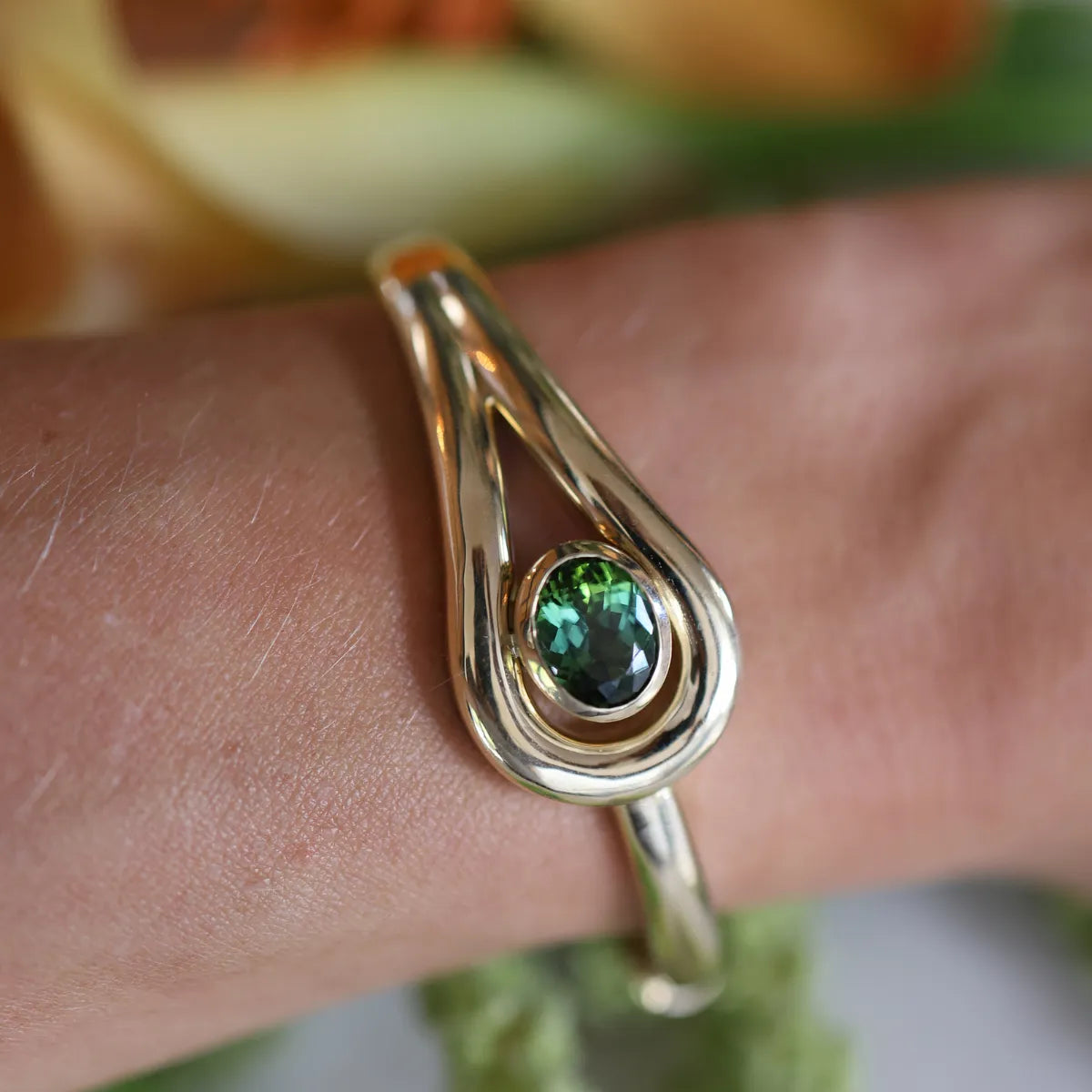 Gold bracelet with a green gemstone on a person's wrist against a blurred natural background