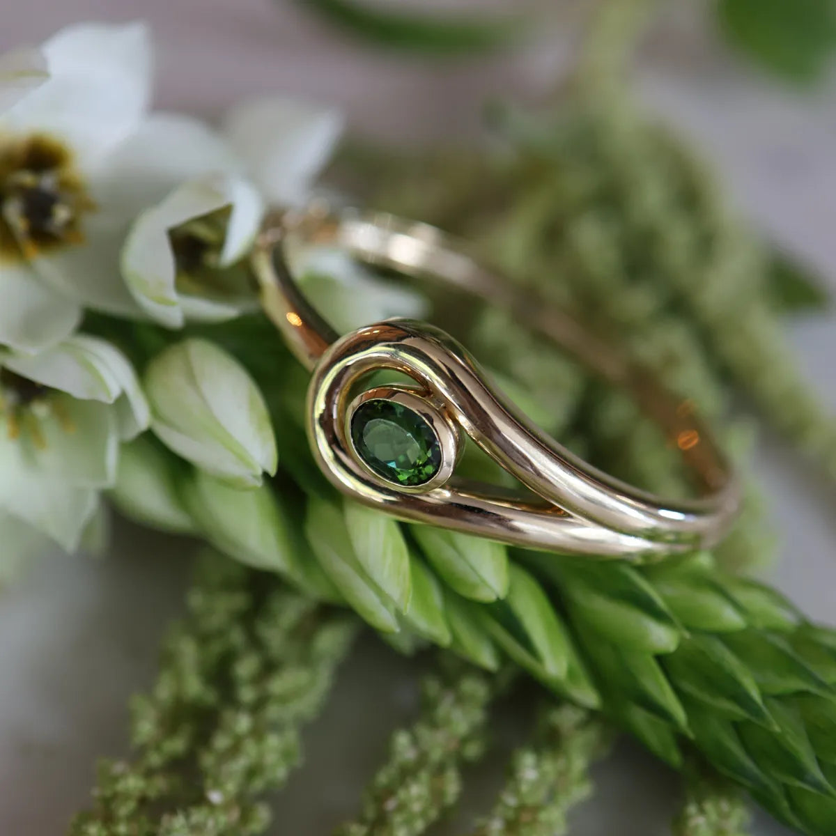 Gold bracelet with a green gemstone on green leaves and white flowers