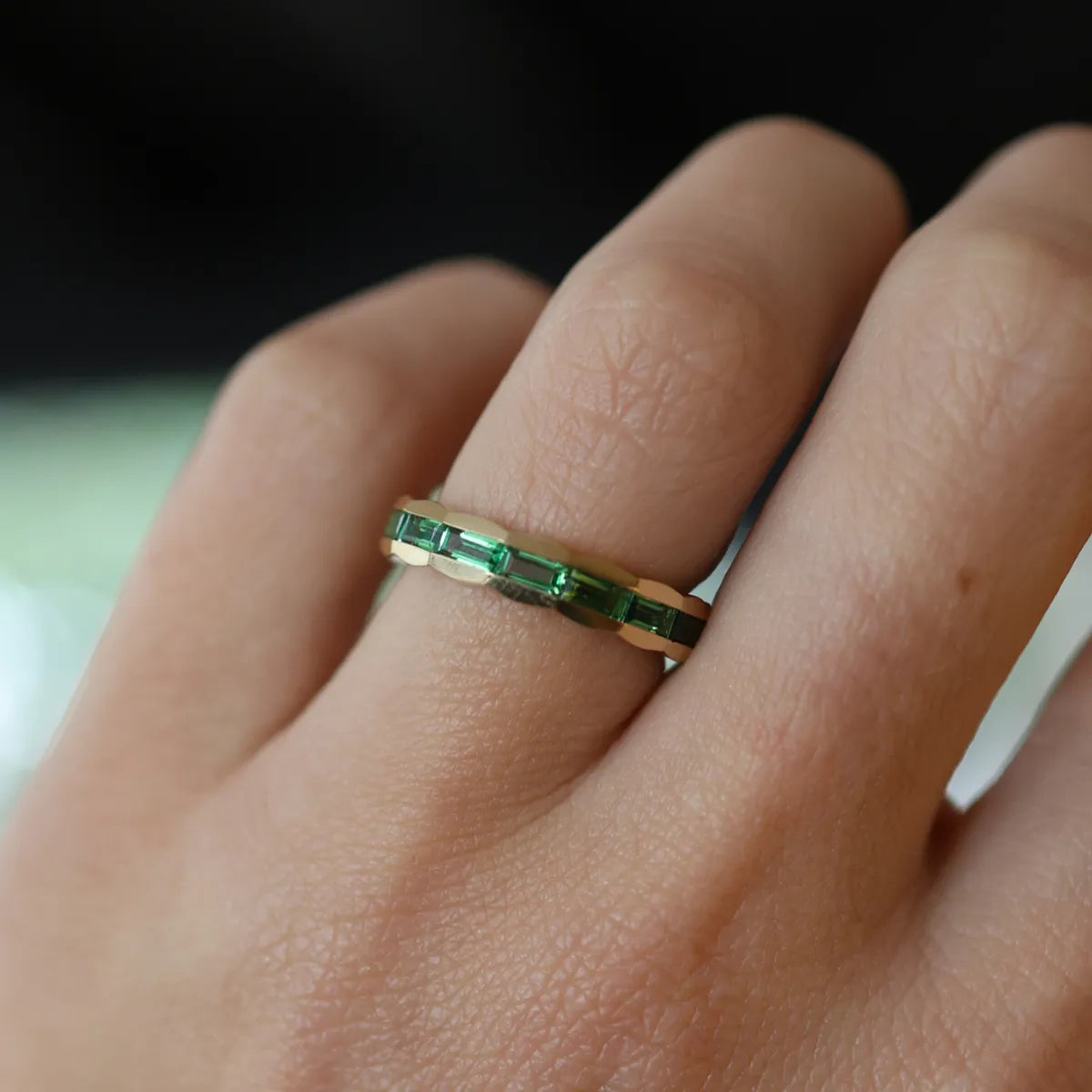 Gold ring with green gemstones on a person's finger against a blurred background
