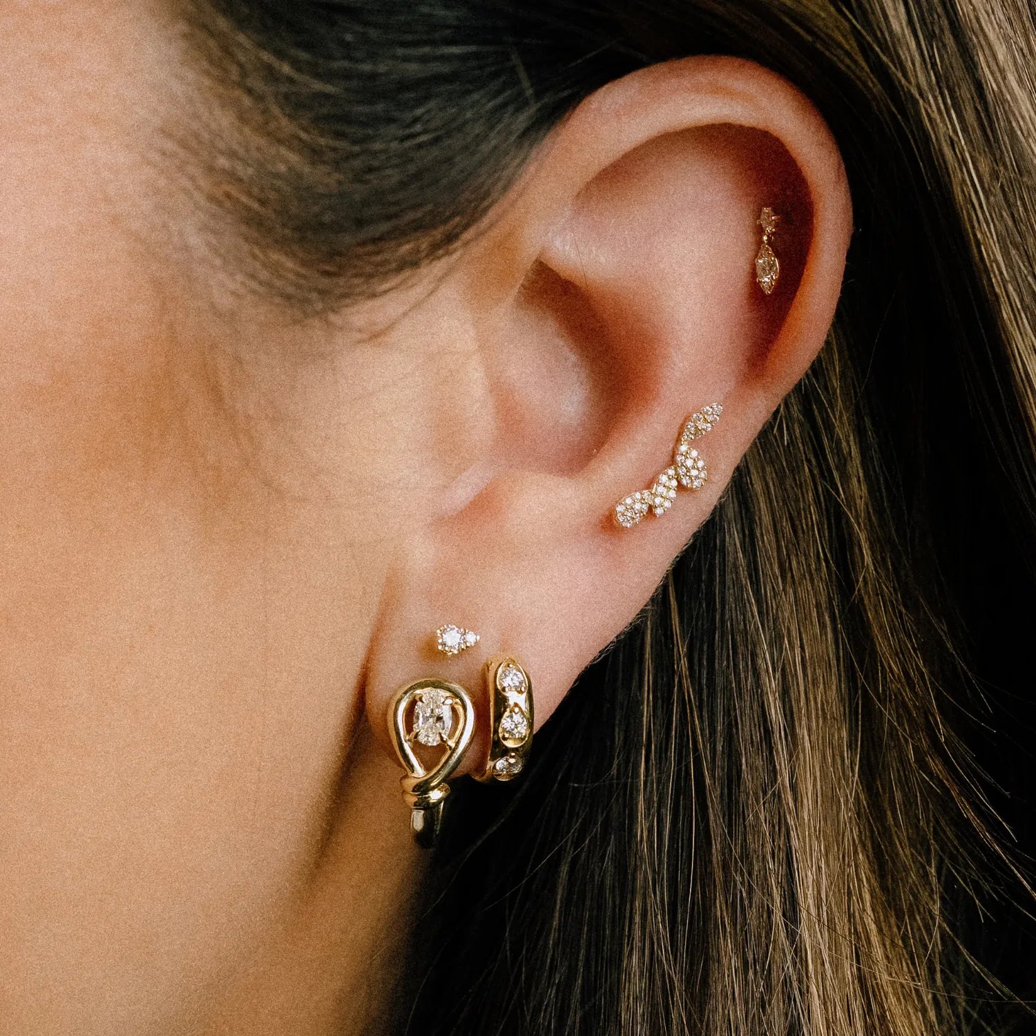 Close-up of an ear wearing gold and diamond earrings.