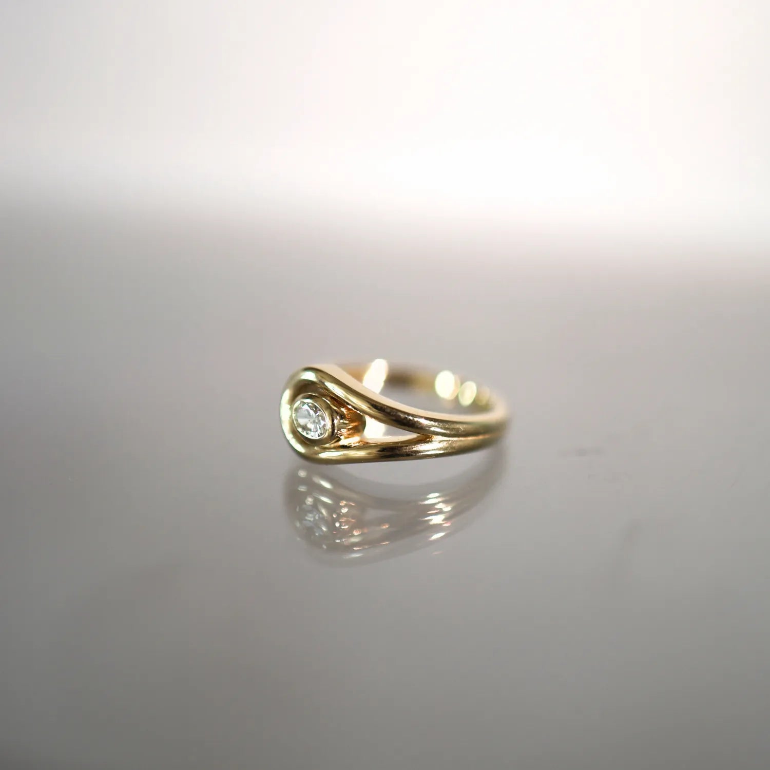Gold ring with a diamond on a reflective gray surface