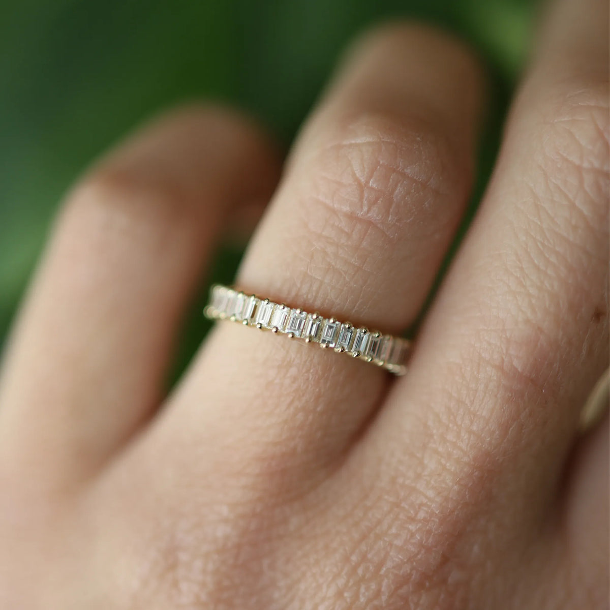 Gold ring with diamonds on a person's finger against a blurred green background