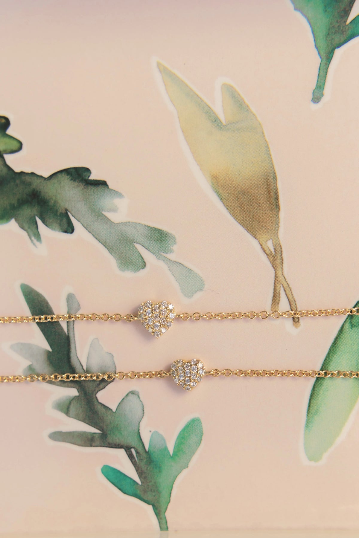 Mom & Babe Matching Diamond Heart Bracelet Set in 18k yellow gold: adult and baby bracelets on a watercolor leaf backdrop