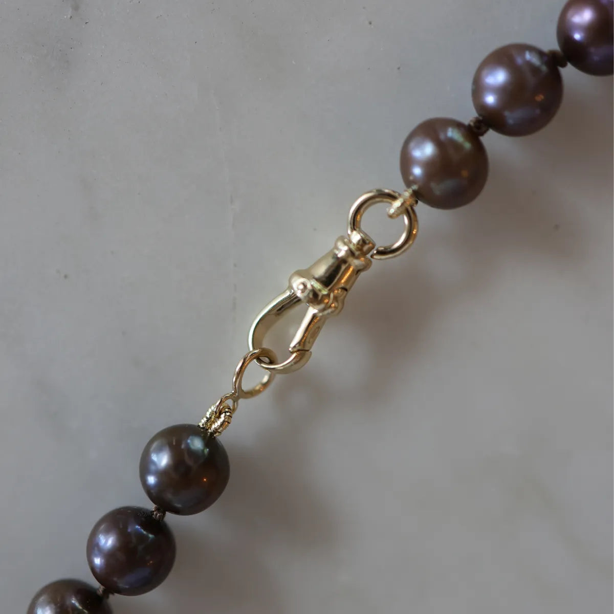 Close-up of a pearl necklace with a gold clasp on a neutral background