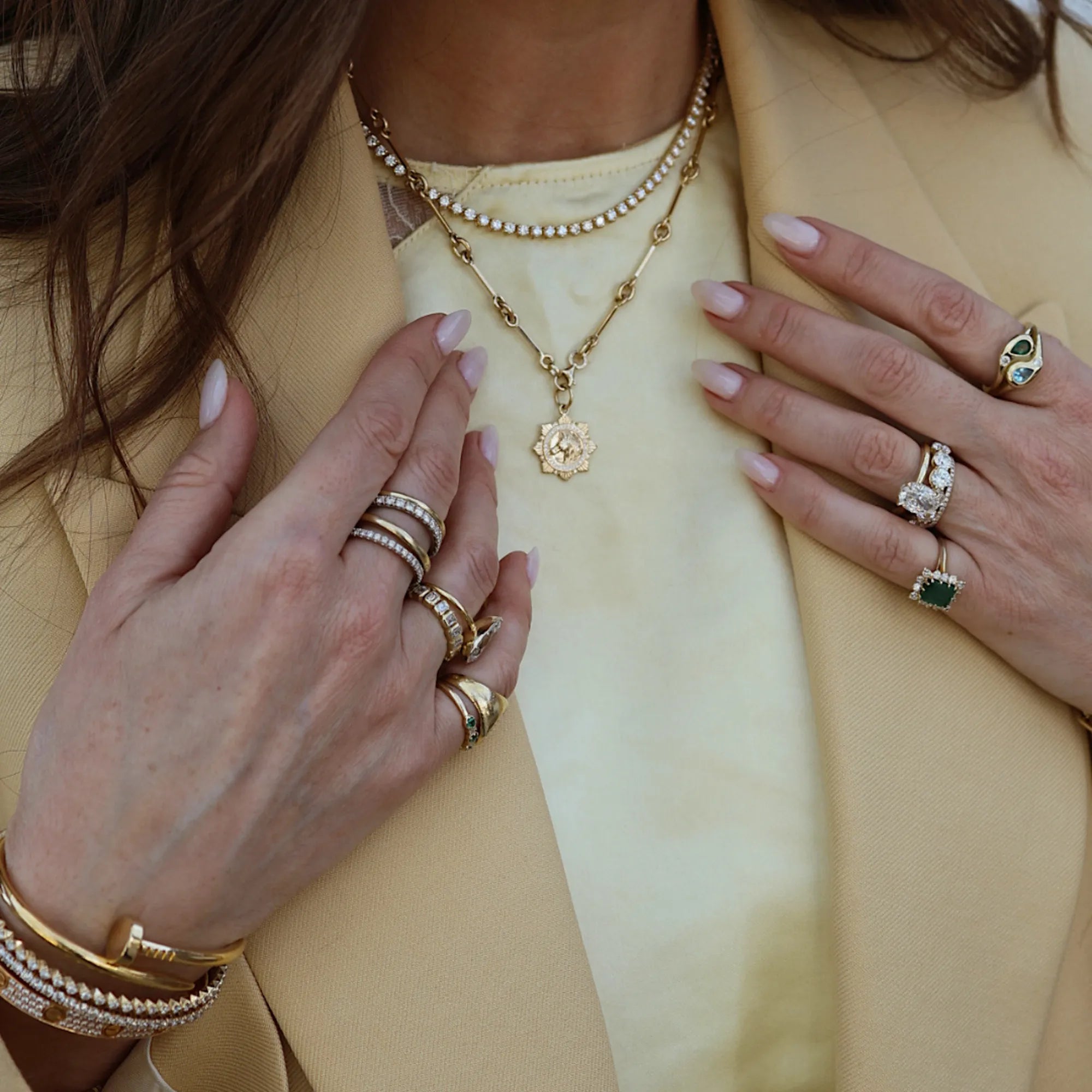 Close-up of hands wearing multiple rings and a necklace with a yellow background