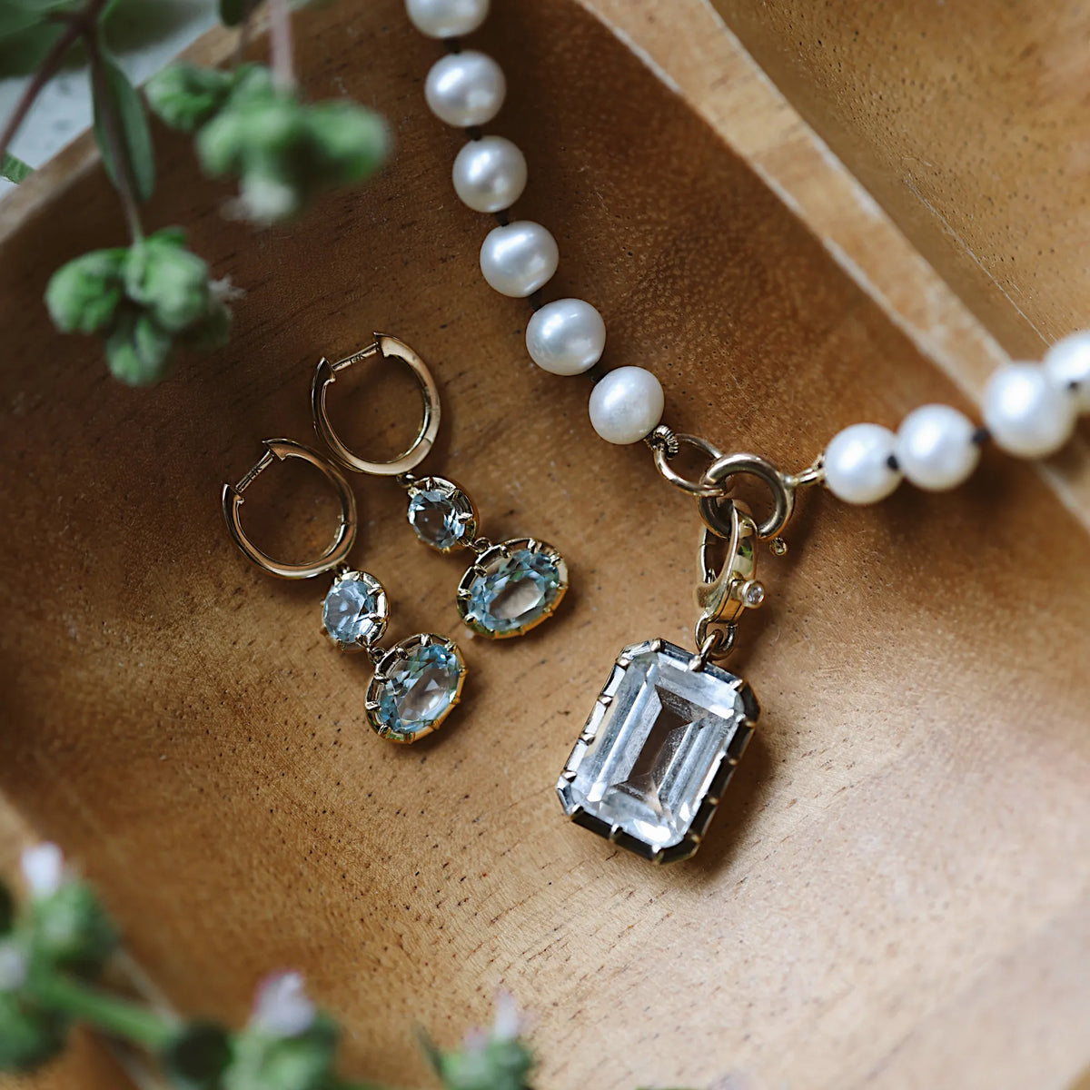 Georgian blue topaz drop earrings in 14k yellow gold styled with freshwater pearl necklace and emerald cut blue topaz pendant, fine jewelry flat lay at Mama Bijoux Costa Mesa