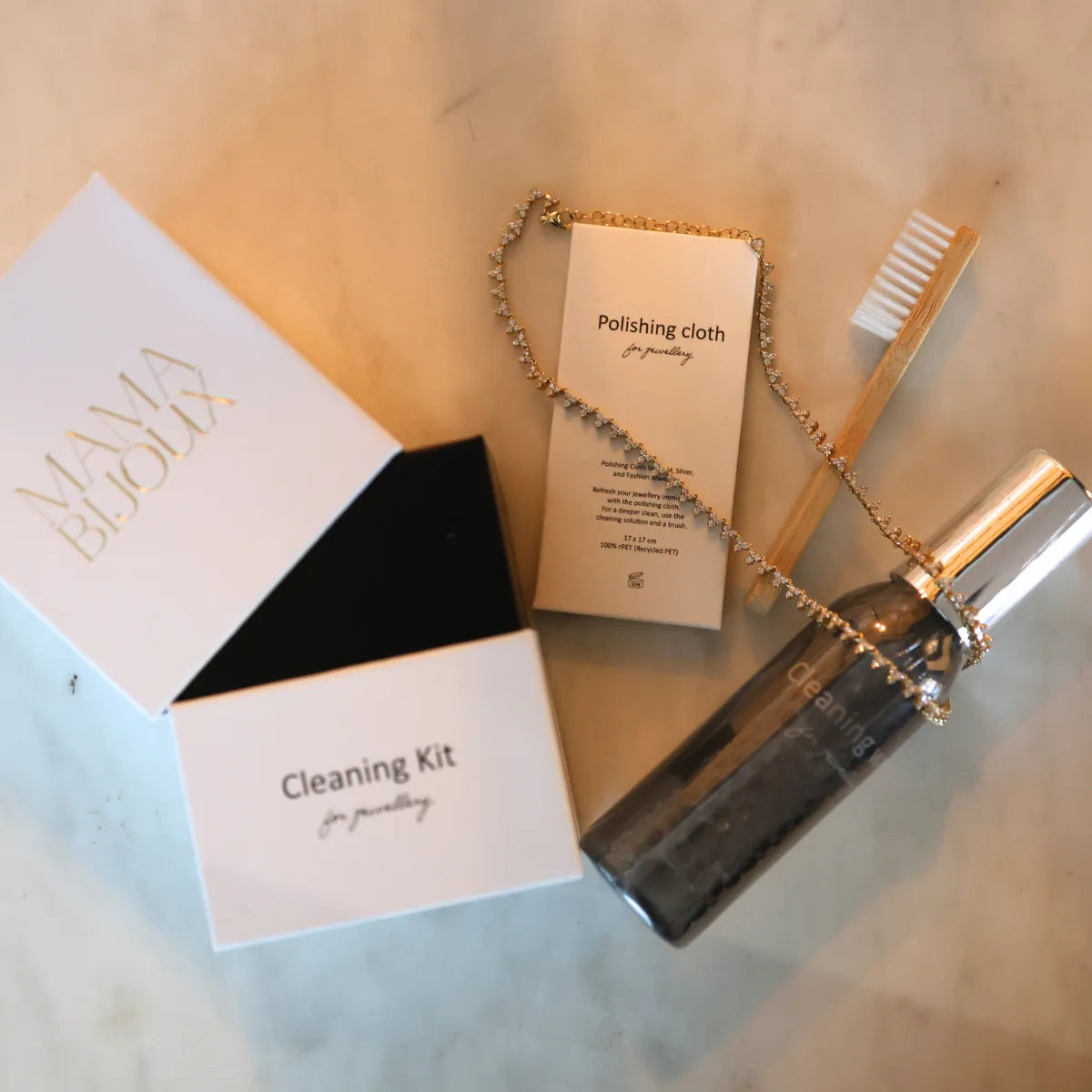 Mama Bijoux premium jewelry cleaning kit with spray solution polishing cloth and soft bristle brush styled with diamond tennis necklace on marble surface