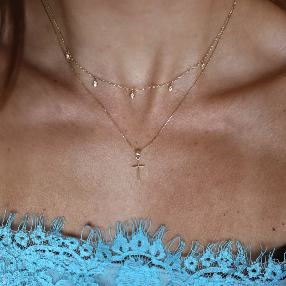 Dainty 14k yellow gold cross charm necklace layered on neck, handmade fine jewelry by Mama Bijoux Costa Mesa Orange County