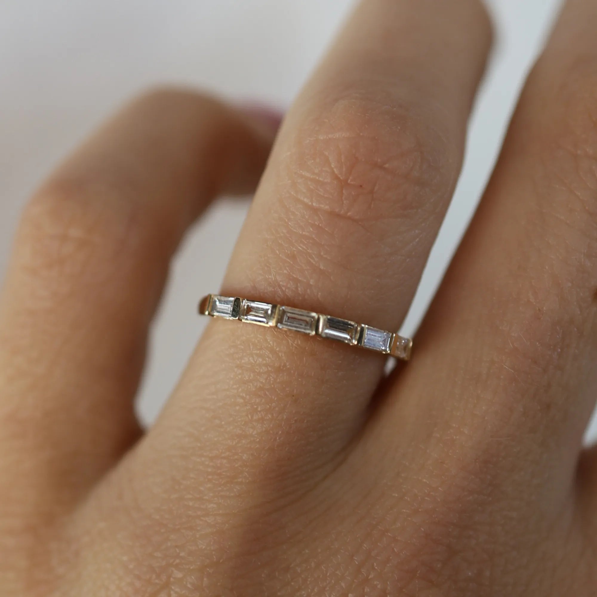 Gold ring with baguette-cut gemstones on a finger against a neutral background