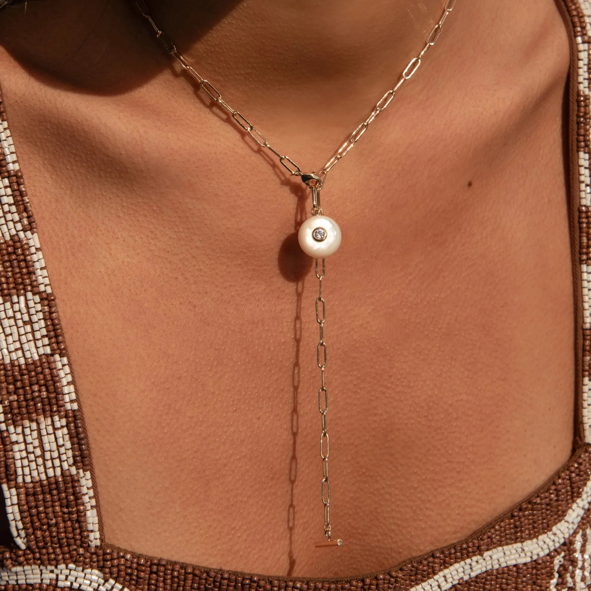 Gold necklace with a pearl pendant on a person wearing a patterned garment.