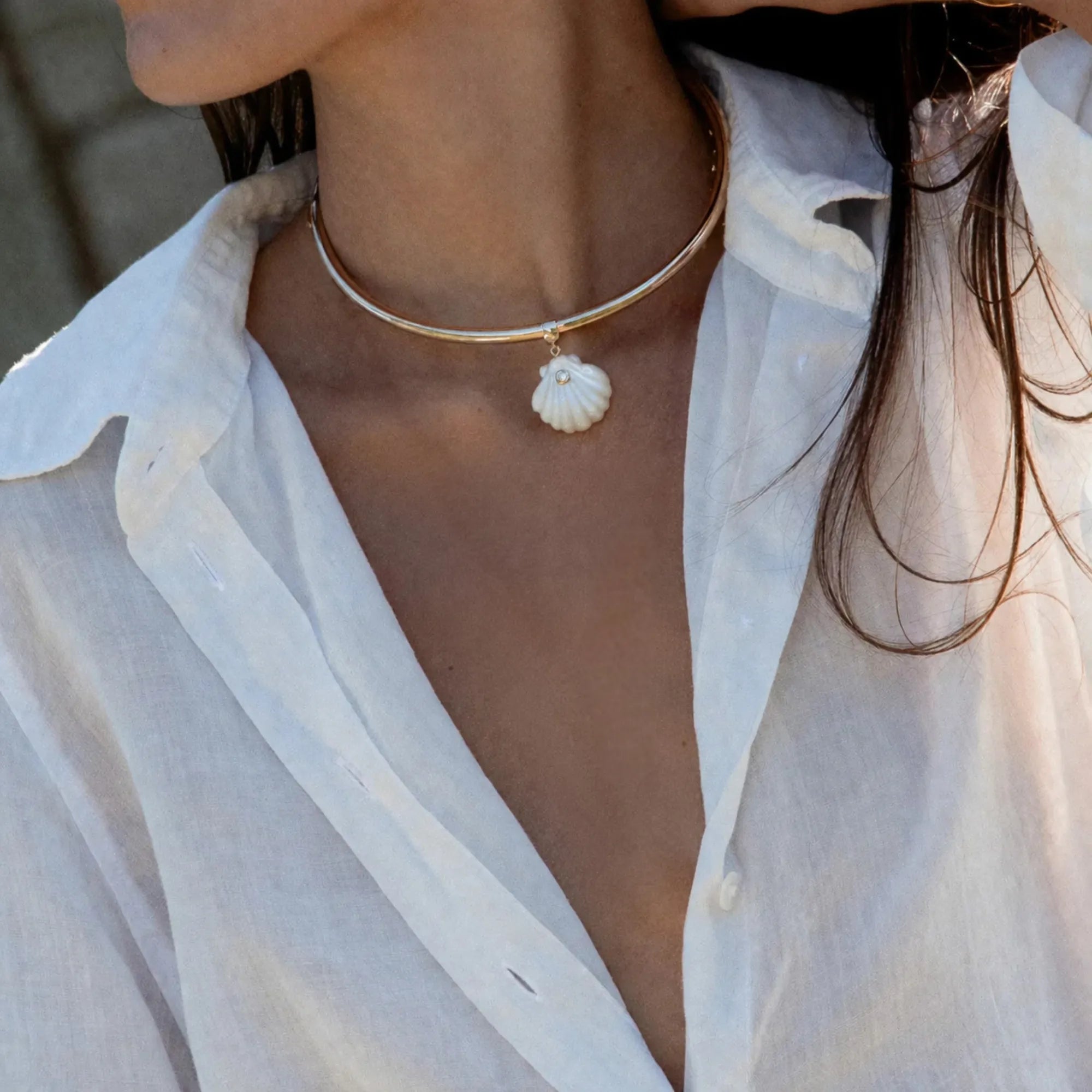 Person wearing a gold necklace with a shell pendant and a white blouse.