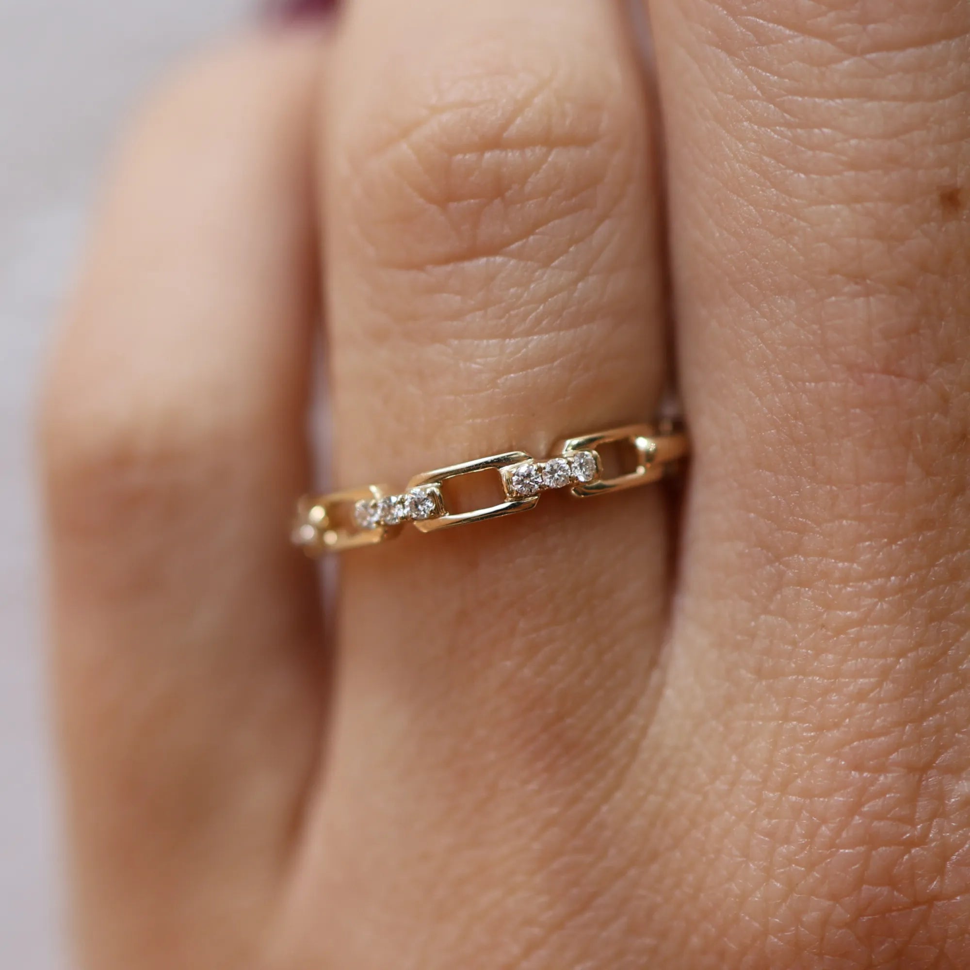 Gold ring with diamonds on a finger against a neutral background