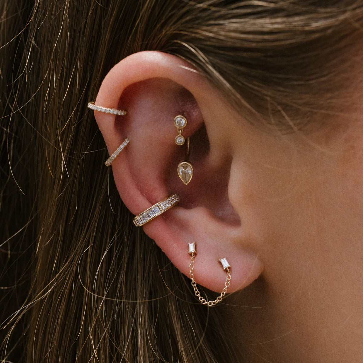 Woman wearing 14k gold baguette diamond chain stud earring in curated ear stack, single stud earring Mama Bijoux