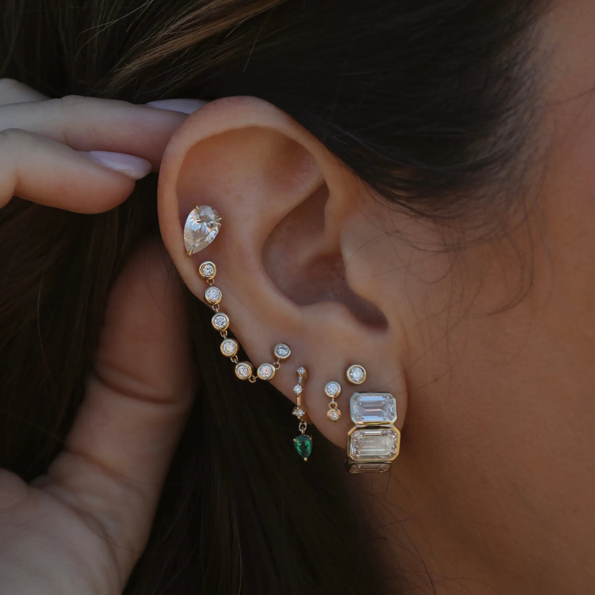 Woman wearing 14k yellow gold emerald cut lab grown emerald huggie earrings styled in an ear stack, Mama Bijoux Orange County fine jewelry
