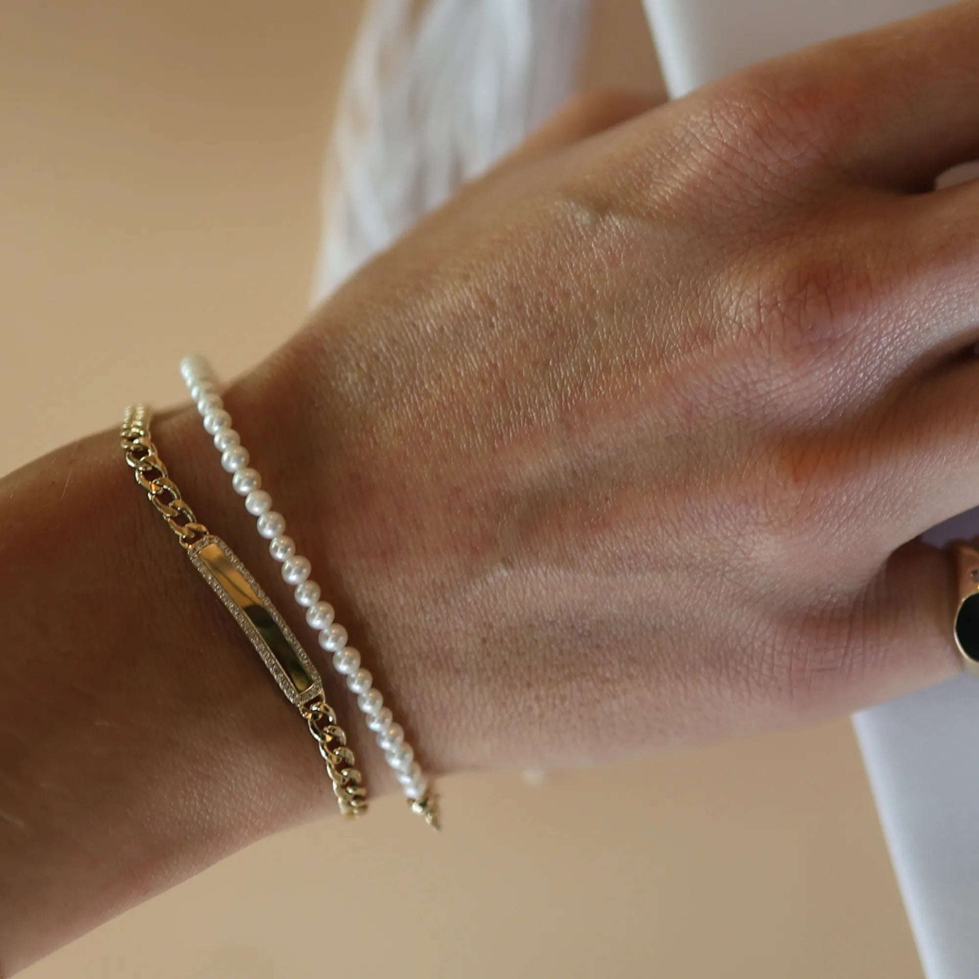 Close-up of a wrist wearing a gold bracelet and pearl bracelet on a neutral background