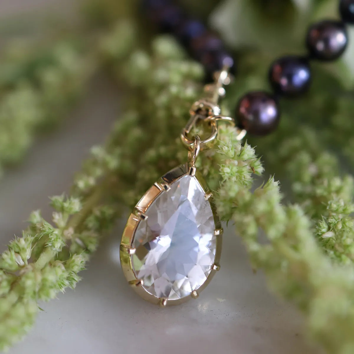 Teardrop-shaped crystal pendant on a gold chain against a natural backgroundmGeorgian Set White Topaz Pear Pendant Floral Photo
