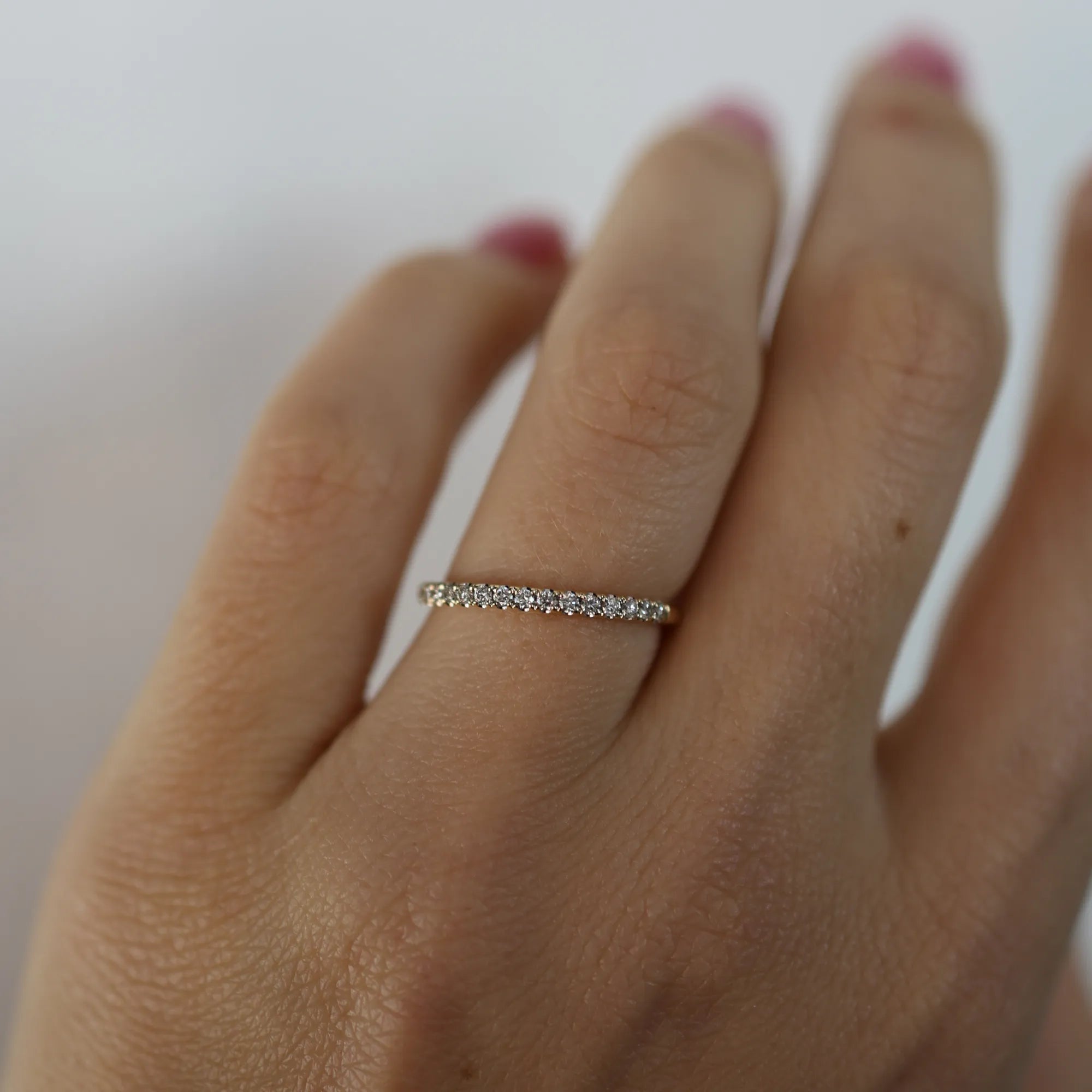 Close-up of a hand wearing a diamond ring on a plain background