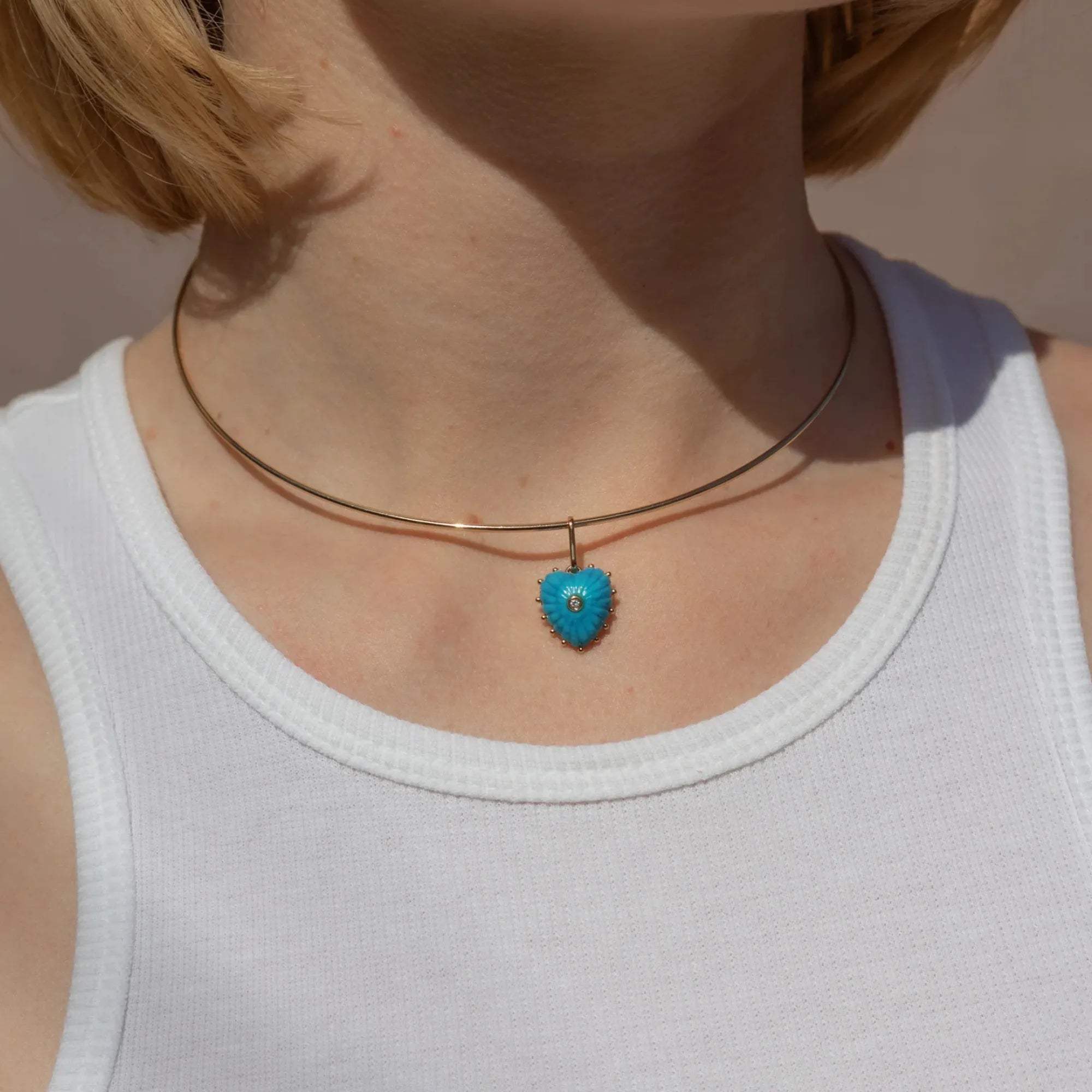 Necklace with a blue heart-shaped pendant worn by a person in a white tank top.