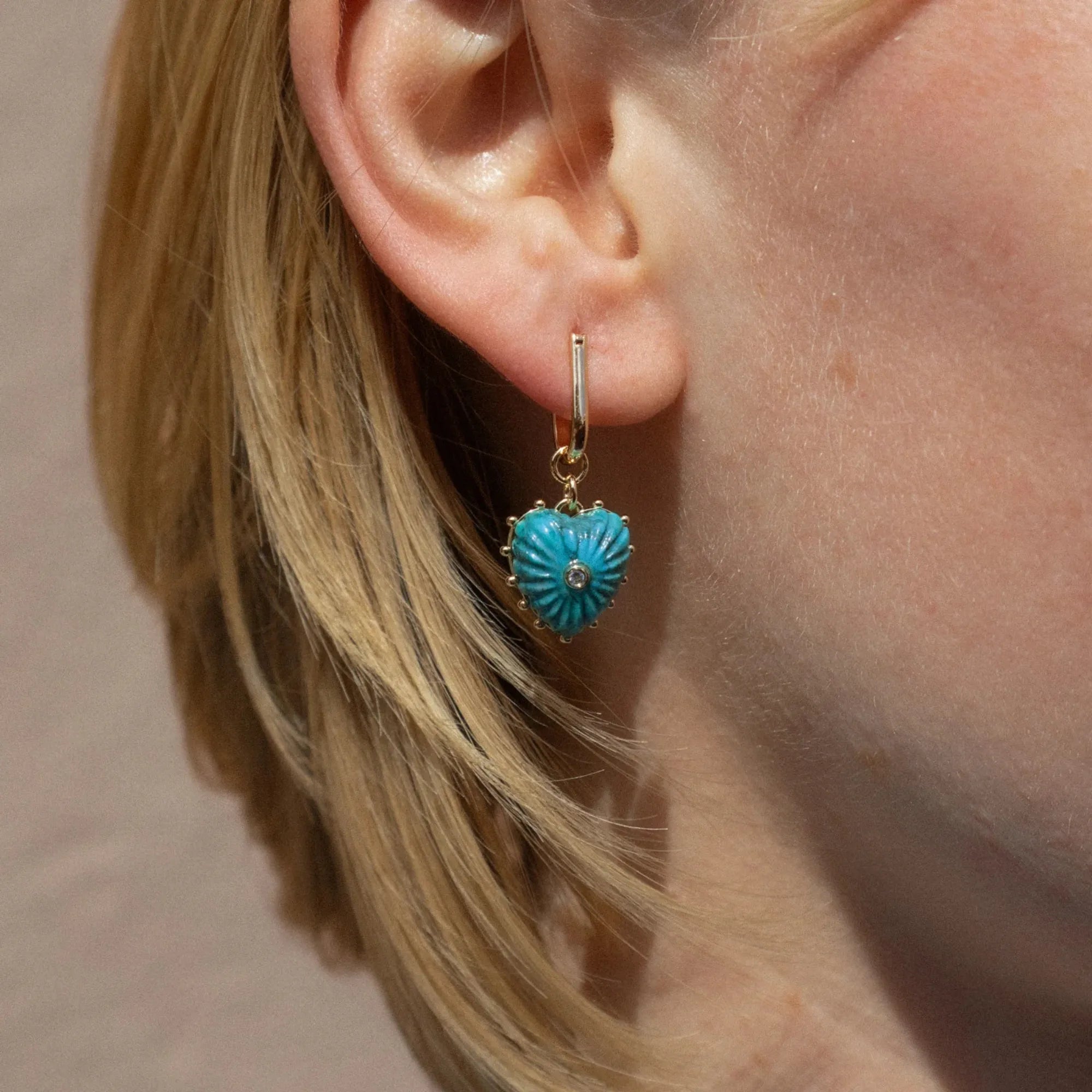 Close-up of a turquoise heart-shaped earring worn by a person with blonde hair.
