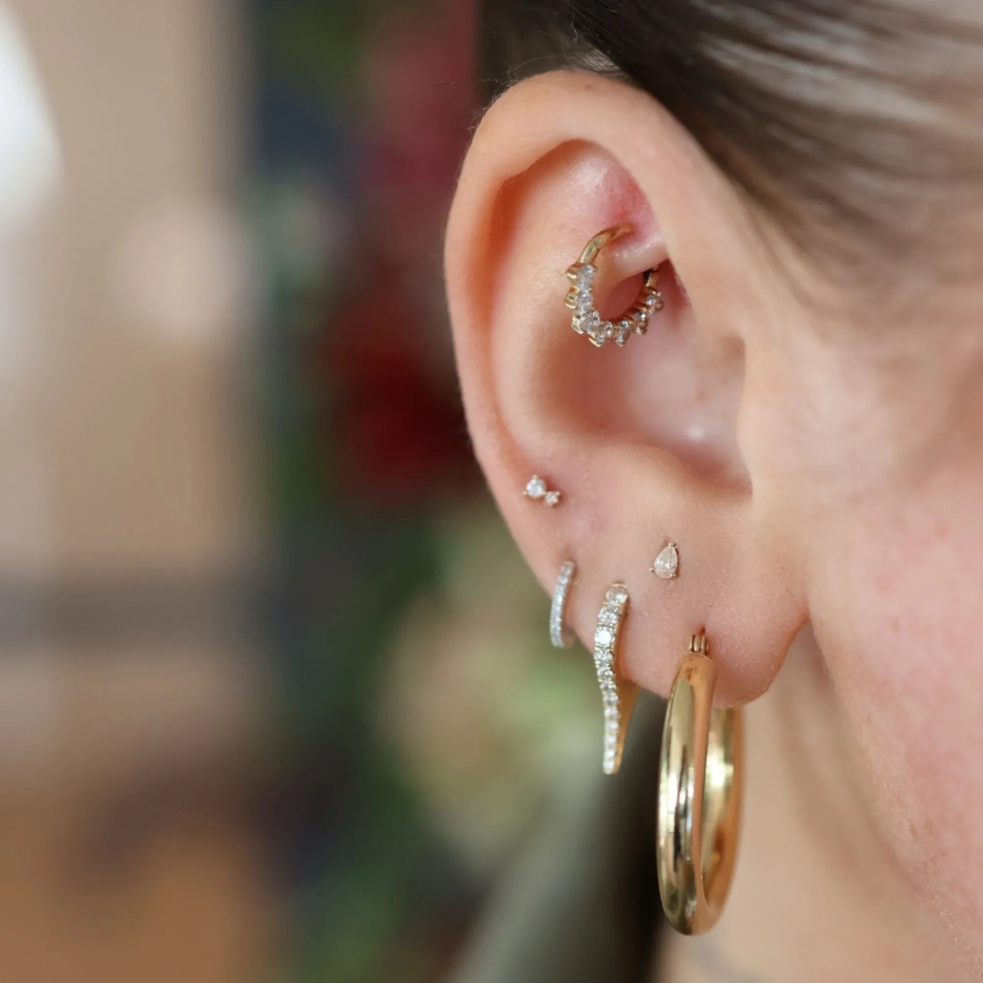 Close-up of an ear with multiple gold and diamond earrings against a blurred background