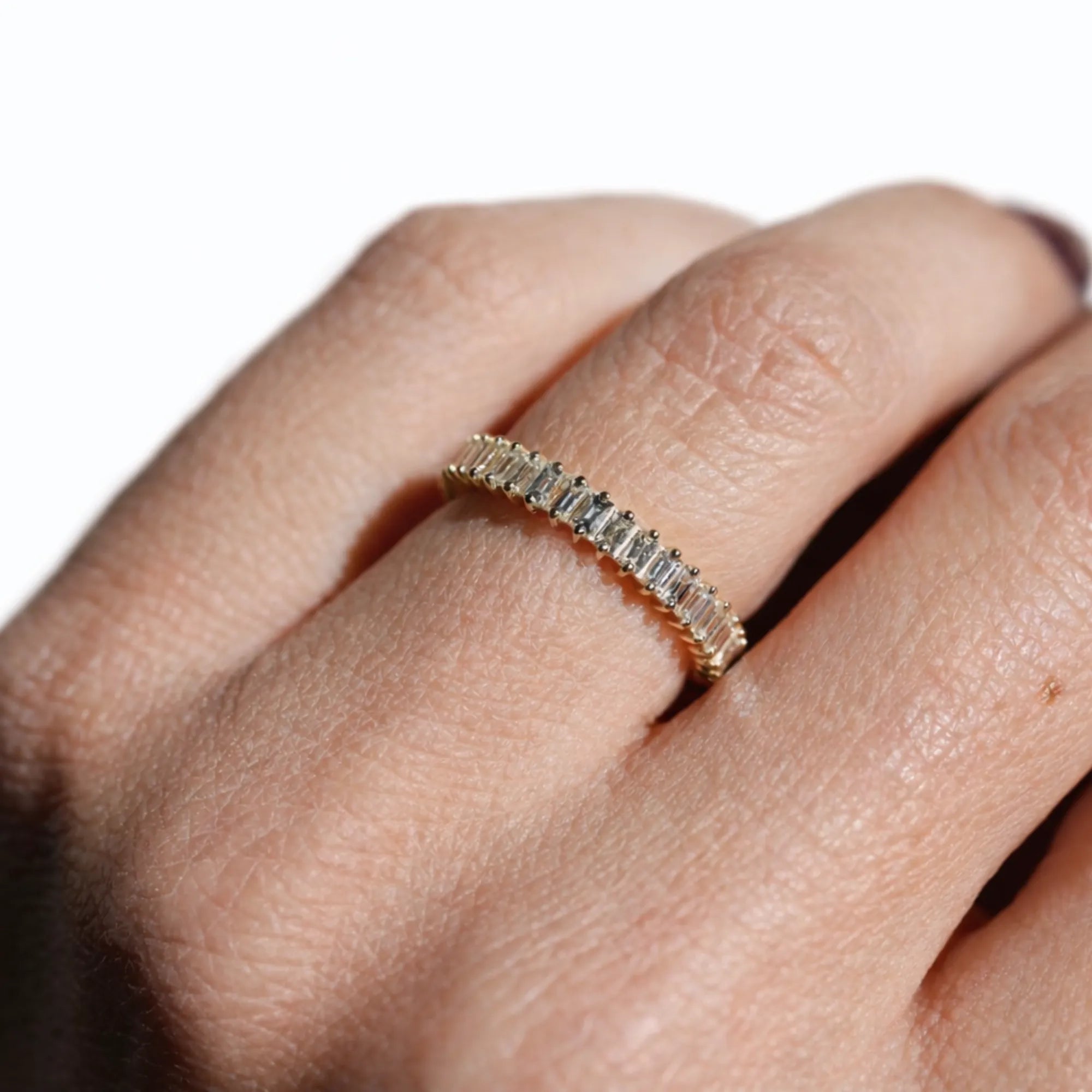 Gold ring with diamonds on a person's finger against a white background