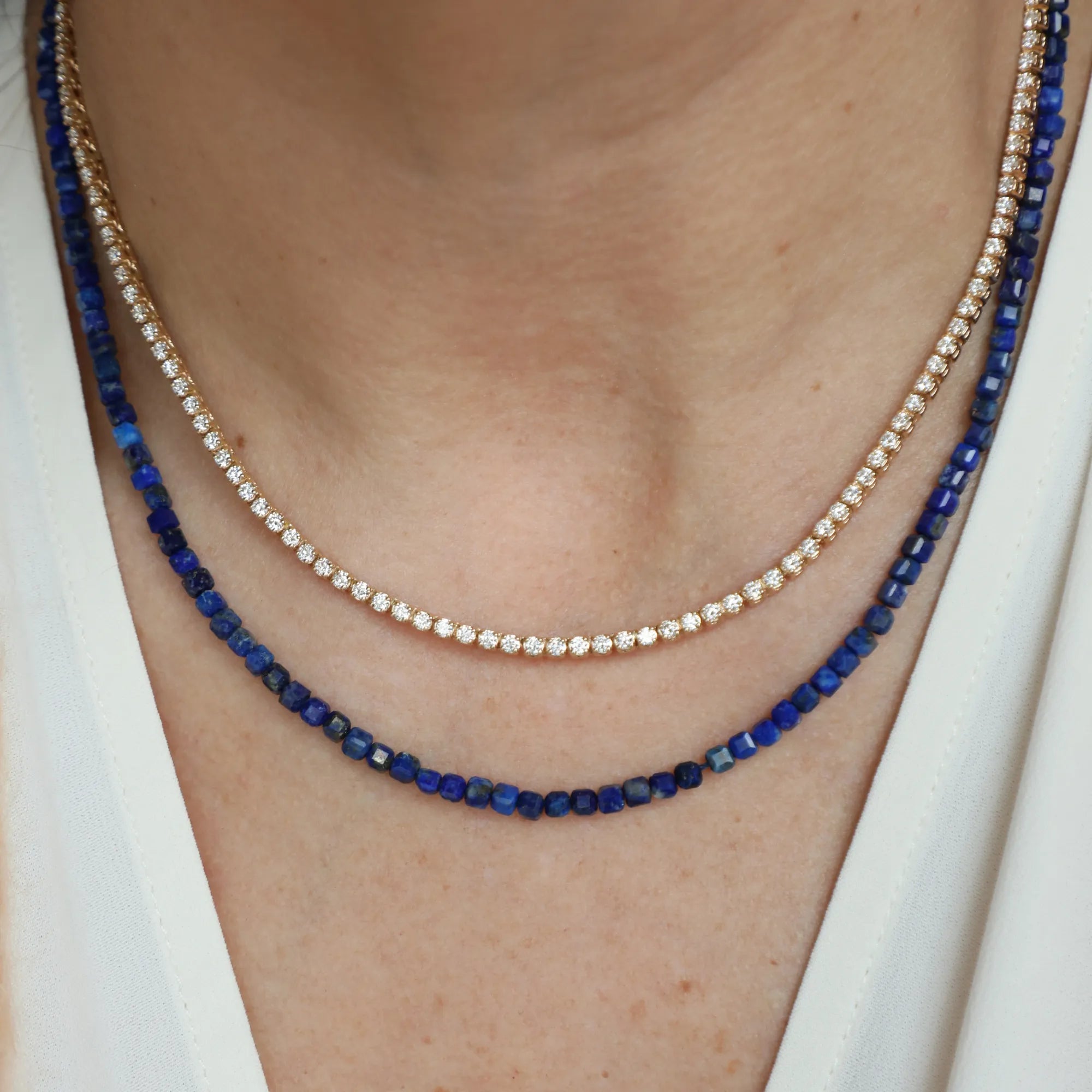 Two necklaces with blue beads and gold chain on a person wearing a white top.
