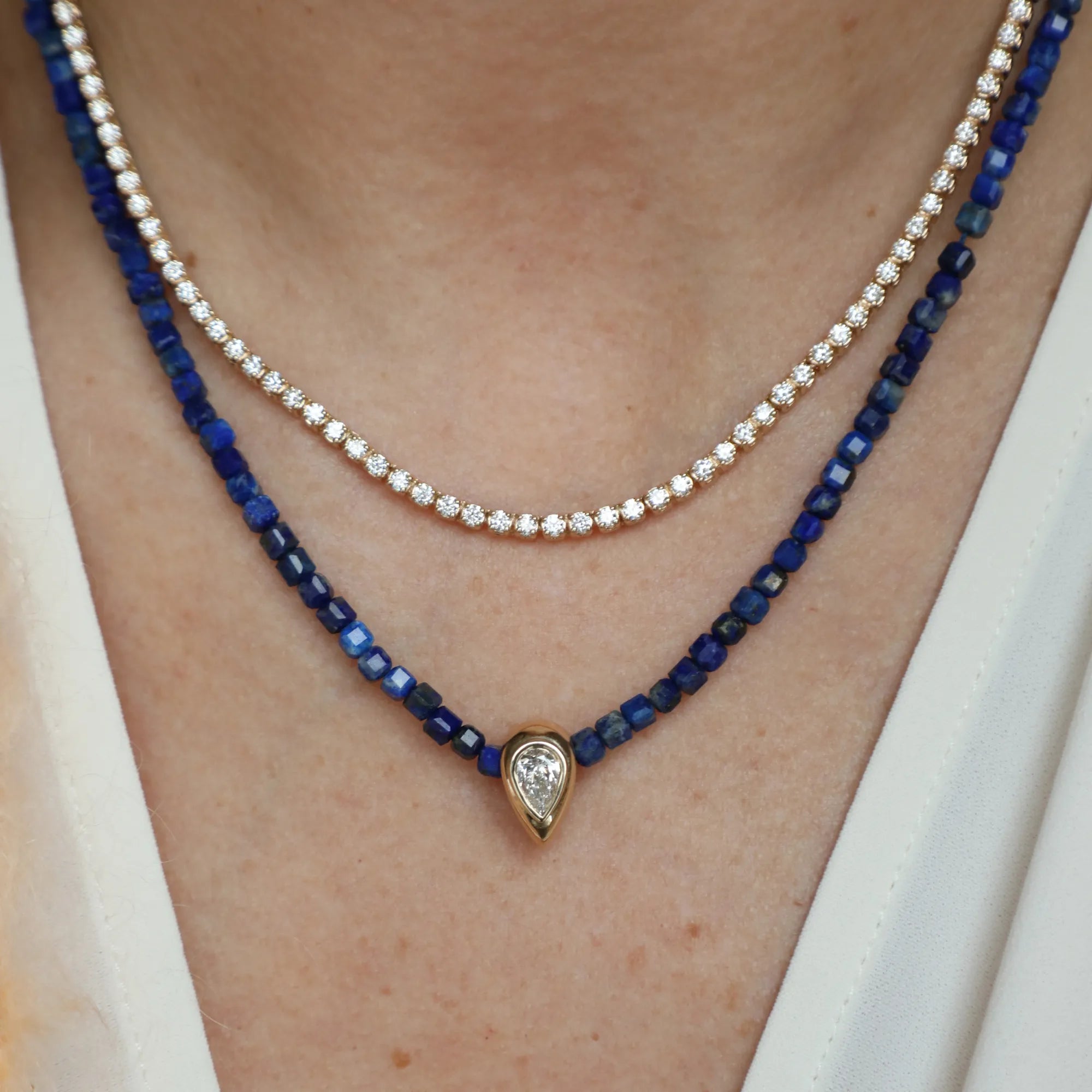 Two necklaces on a person's neck, one with blue beads and a gold heart pendant, the other with white beads.