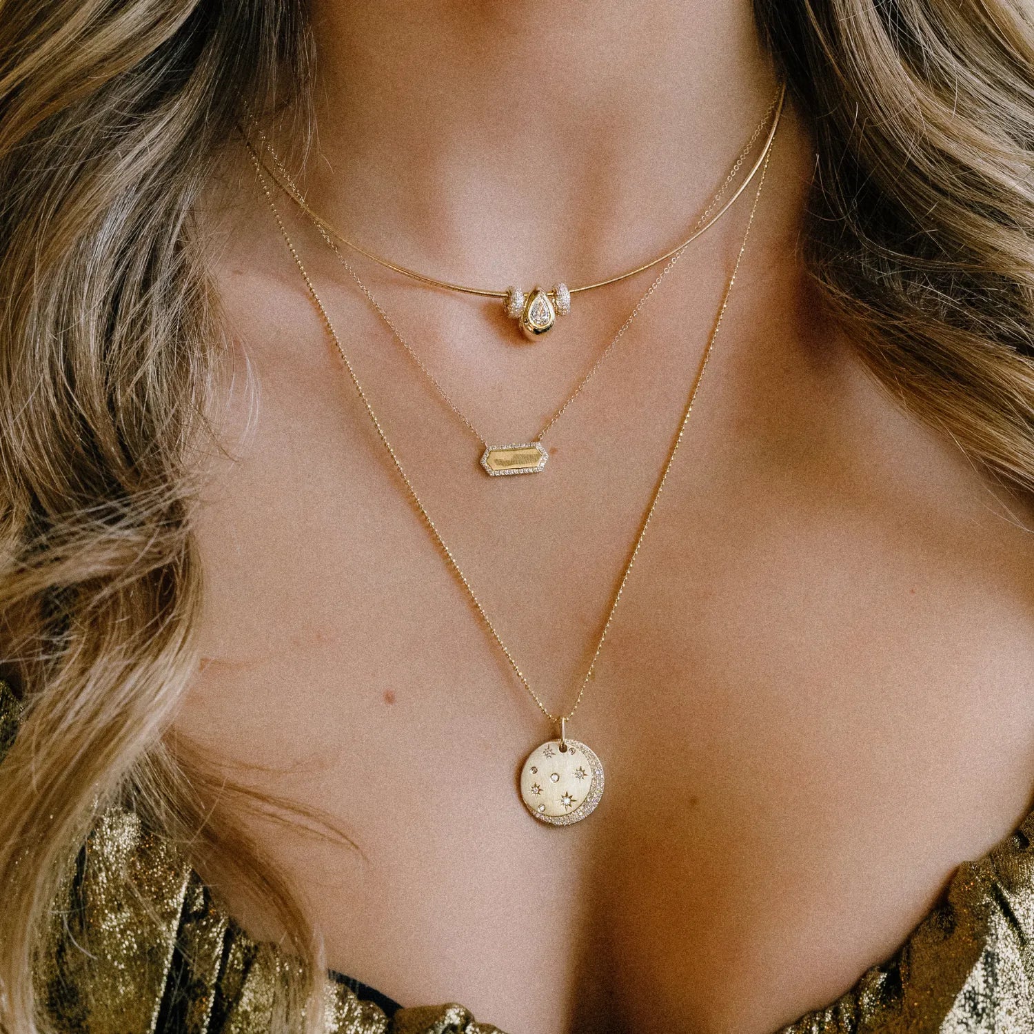 Close-up of a woman wearing multiple gold necklaces with various pendants.