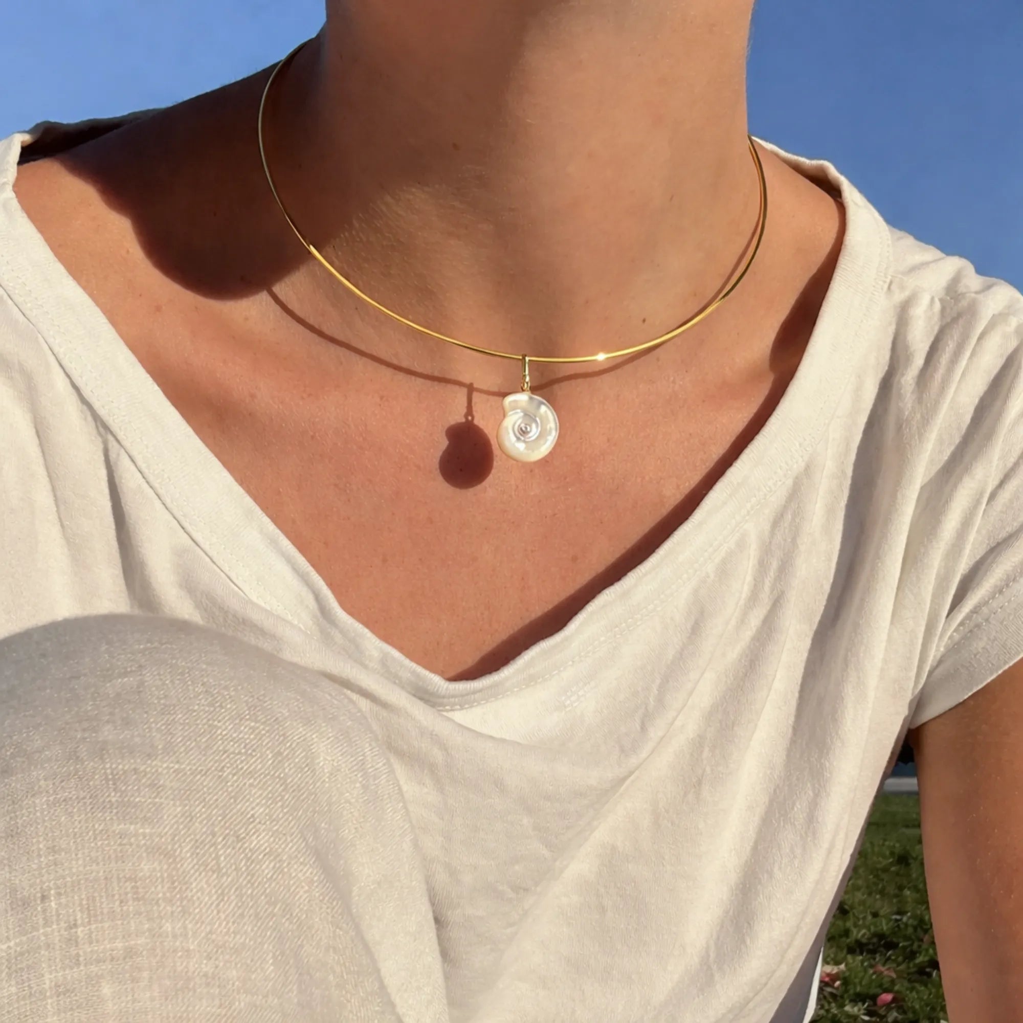Necklace with a pendant worn by a person against a blue sky.