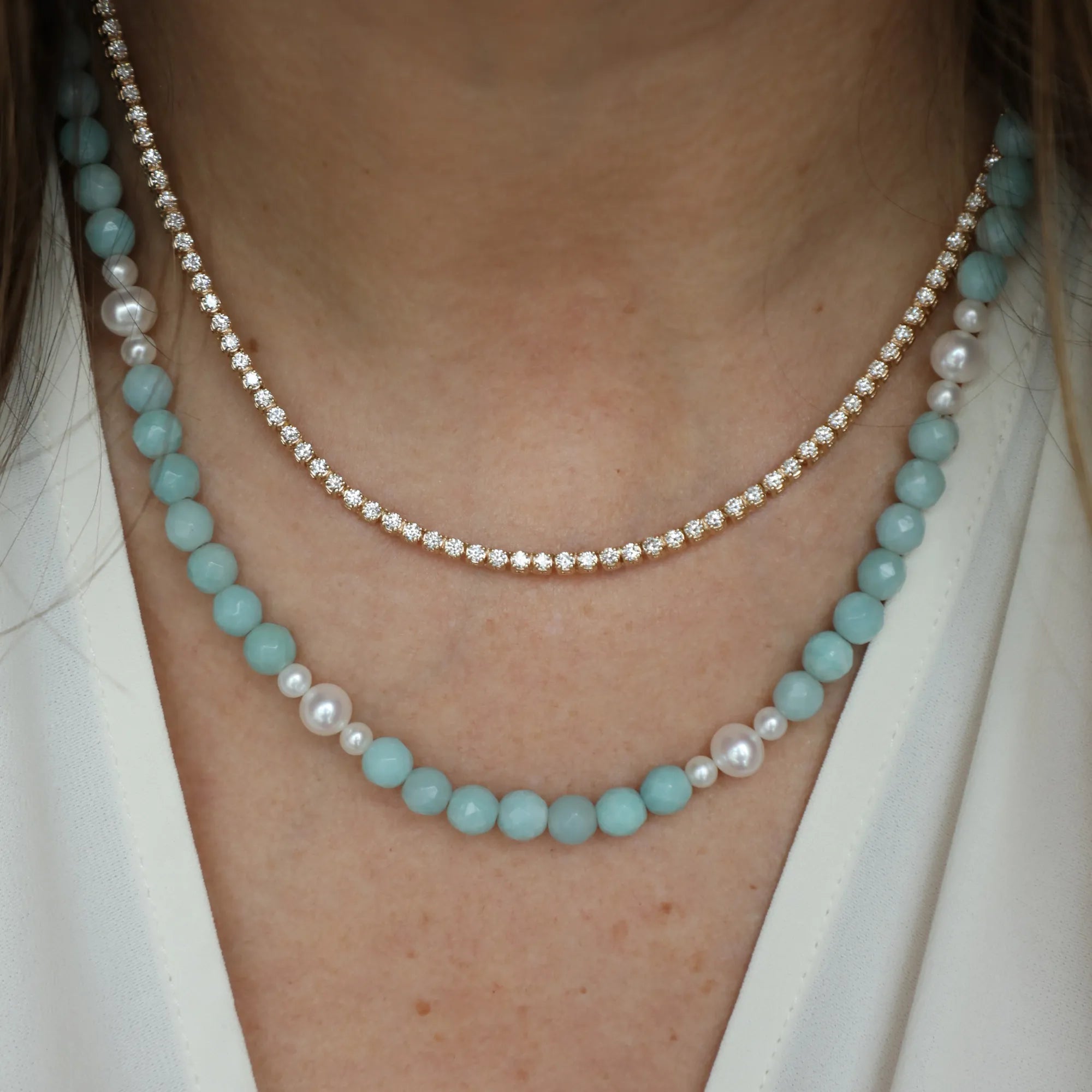 Two necklaces on a person's neck, one with turquoise beads and the other with pearls.