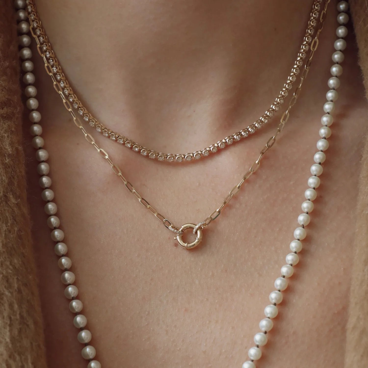 Two pearl necklaces and a gold chain necklace on a person's neck against a neutral background.
