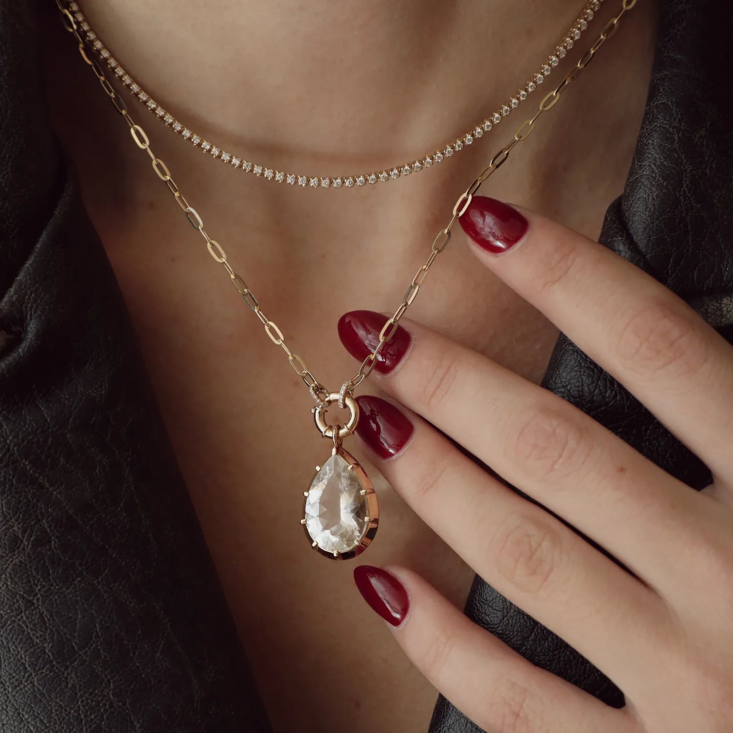 Necklace with a teardrop-shaped pendant worn by a person with red nail polish.