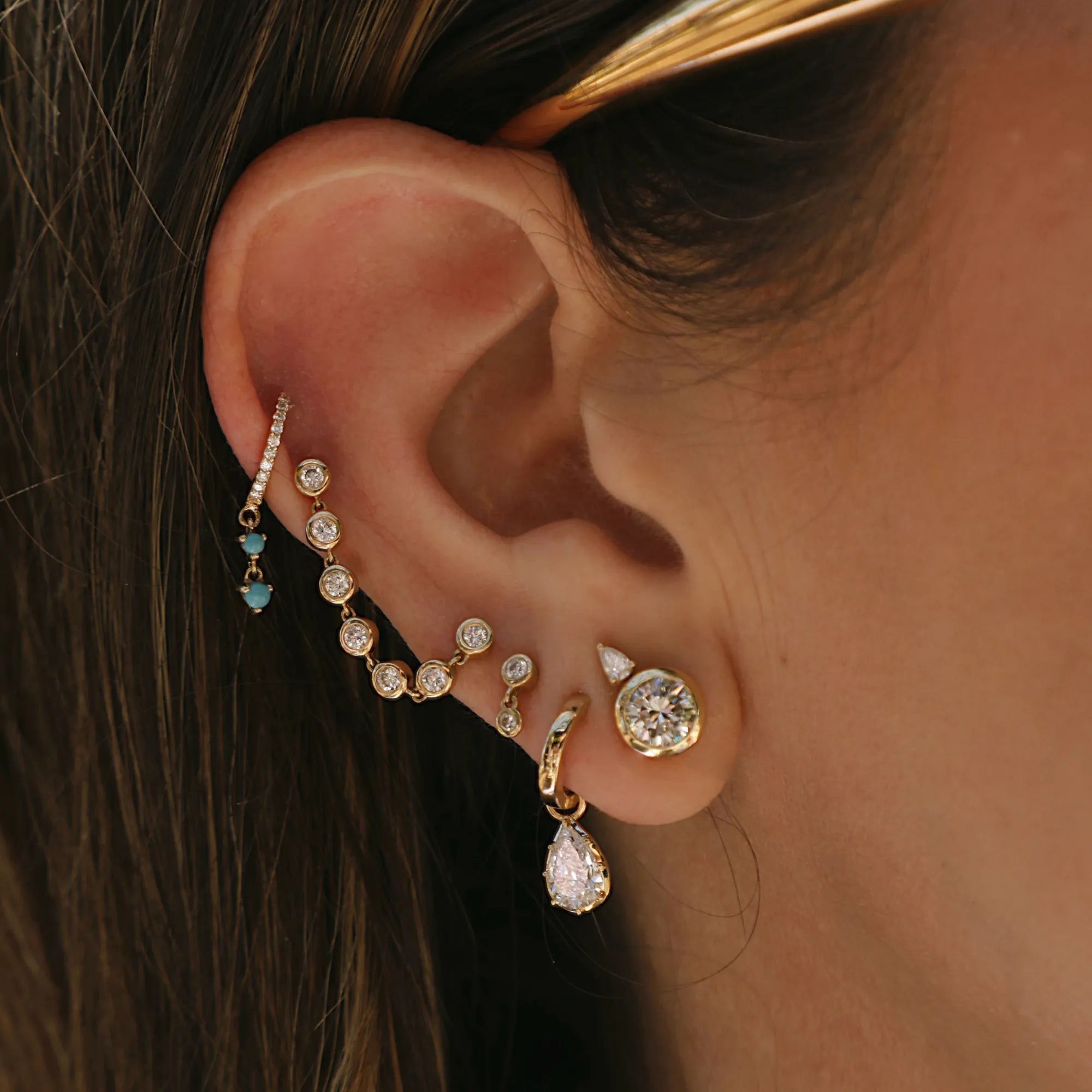 Dainty gold ear cuff with diamond chain earrings and turquoise accents in a curated luxury ear stack styling.