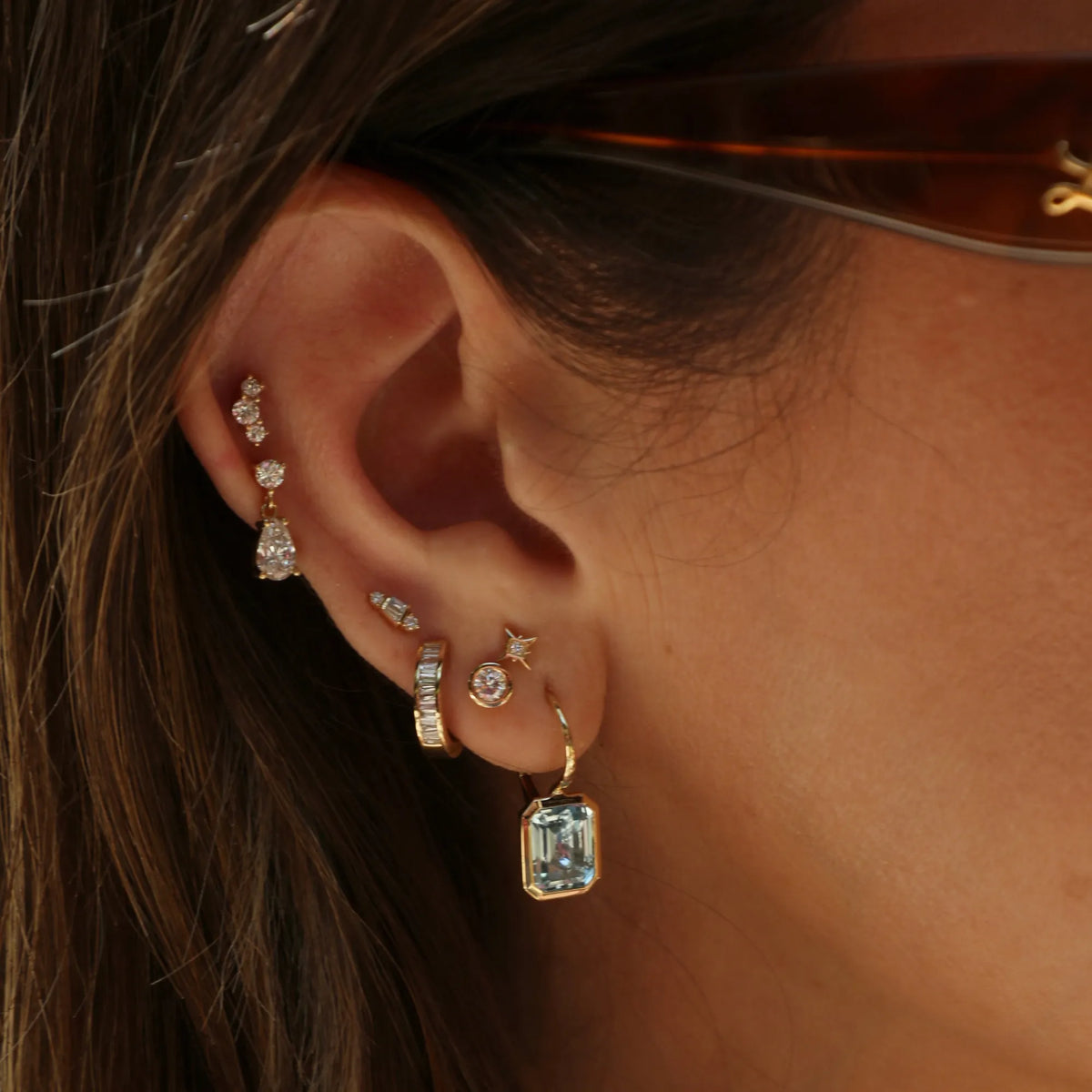 Woman wearing emerald cut blue topaz drop earrings with bezel-set gemstones, styled as sophisticated luxury fine jewelry