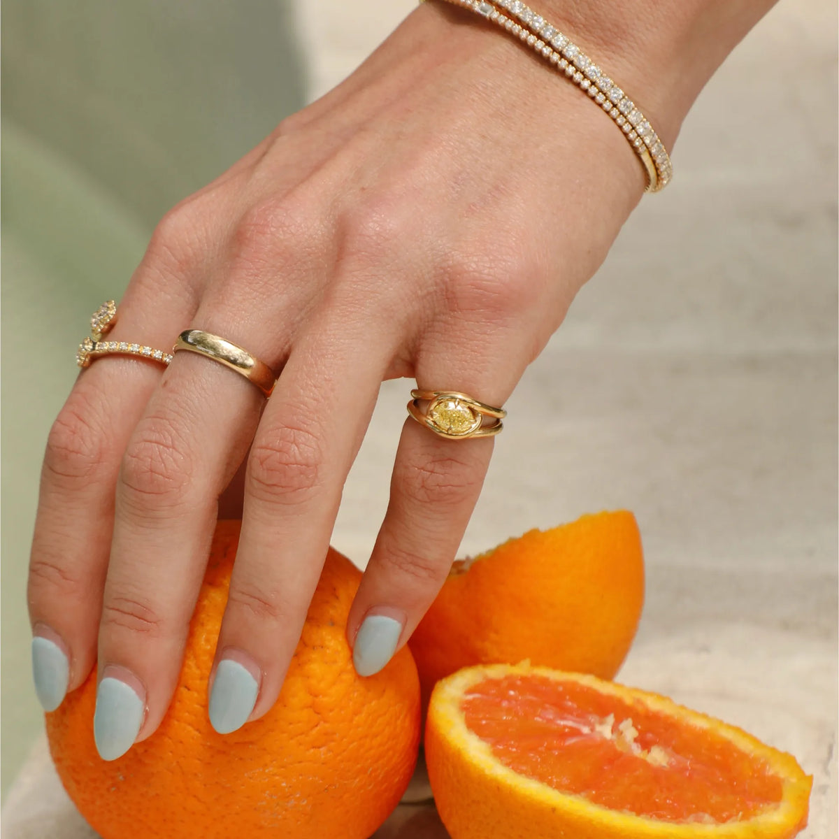 Yellow lab diamond pinky ring stacked with gold diamond bands and a diamond tennis bracelet, styled with citrus fruit for a summer jewelry editorial, Mama Bijoux Orange County